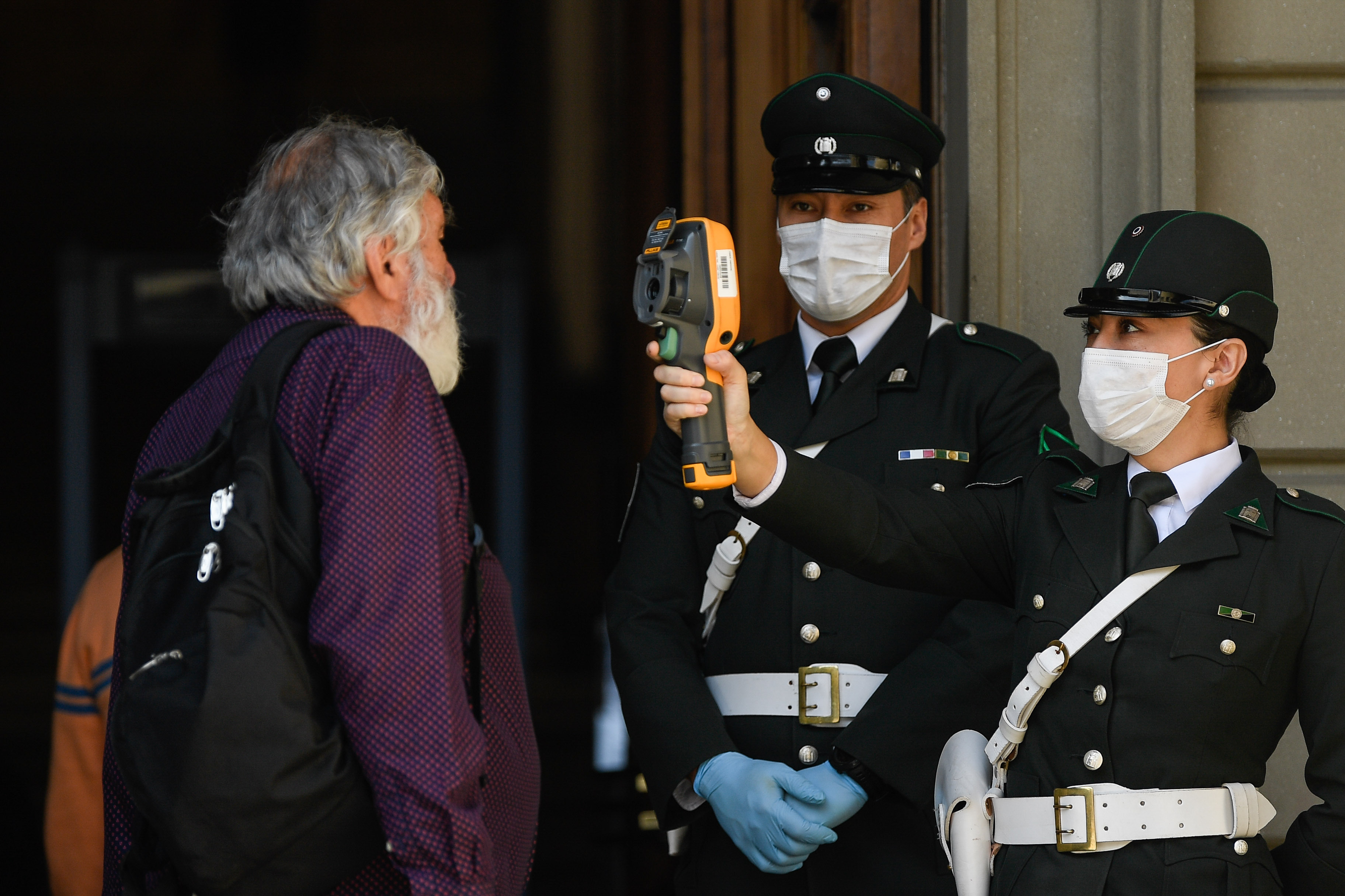 3月20日,在智利圣地亚哥司法大楼外站岗的警察为访客测量体温.