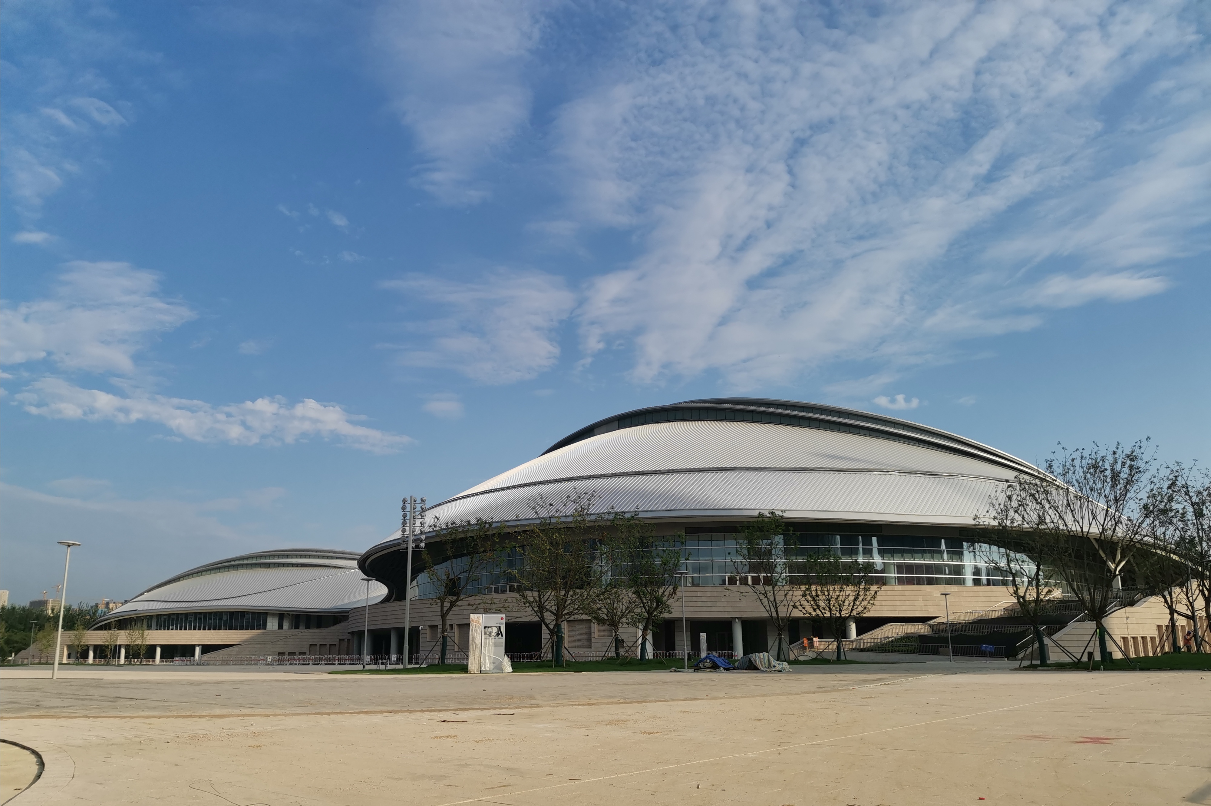 体育馆以灵动飘逸的银色屋面融合曲线平台,多级步道及双层柱廊等立面