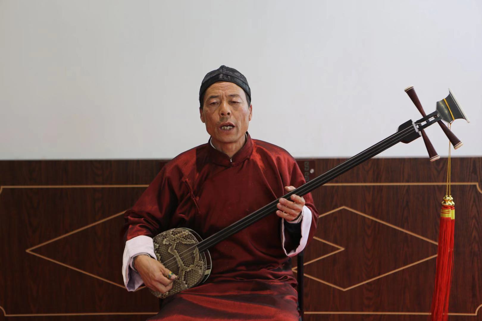 武威市凉州区文化馆里,54岁的董永虎一身红袍,怀抱三弦,正弹唱一段贤